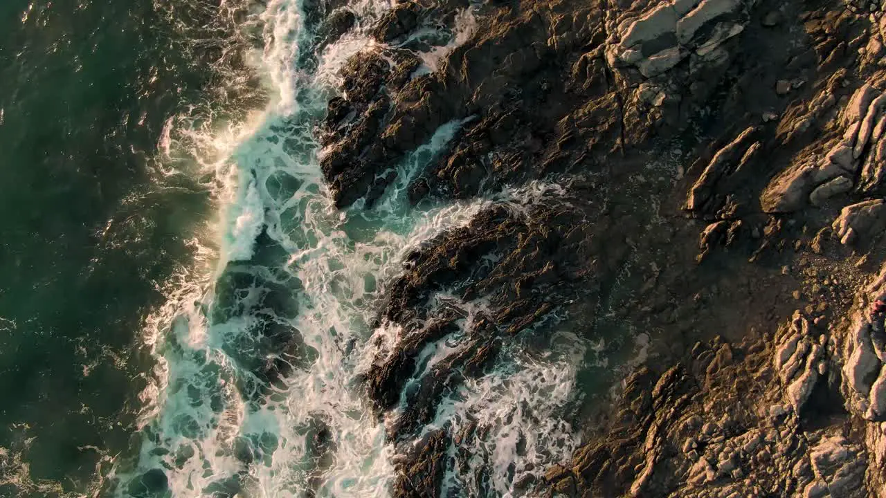 Drone top down crane shot of breaking waves on rocky Costa Rica beach in sunset