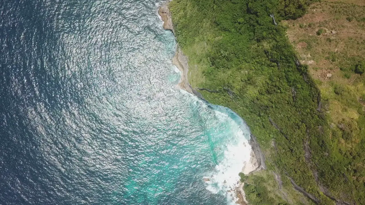 Aerial straight down Green jungle cliffs protect warm turquoise water