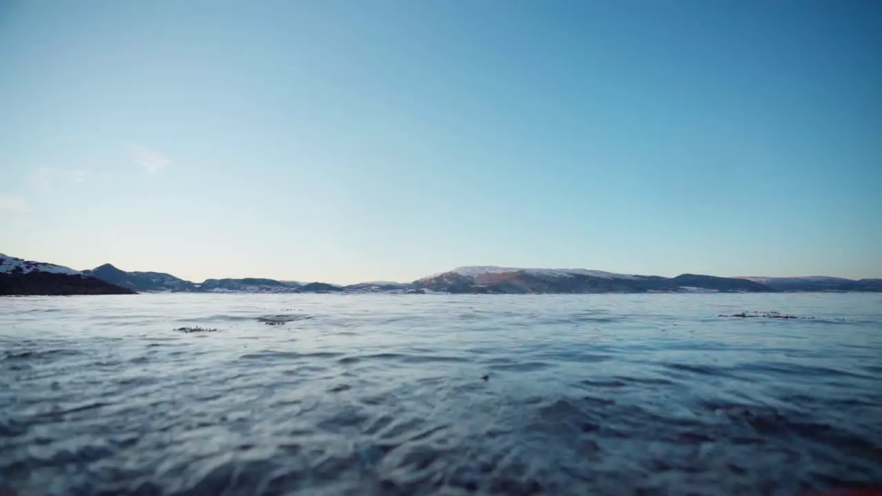 A Pet Dog With A Red Rope Walking On The Beach Shore With View Of Blue Summer Sky Over The Mountains