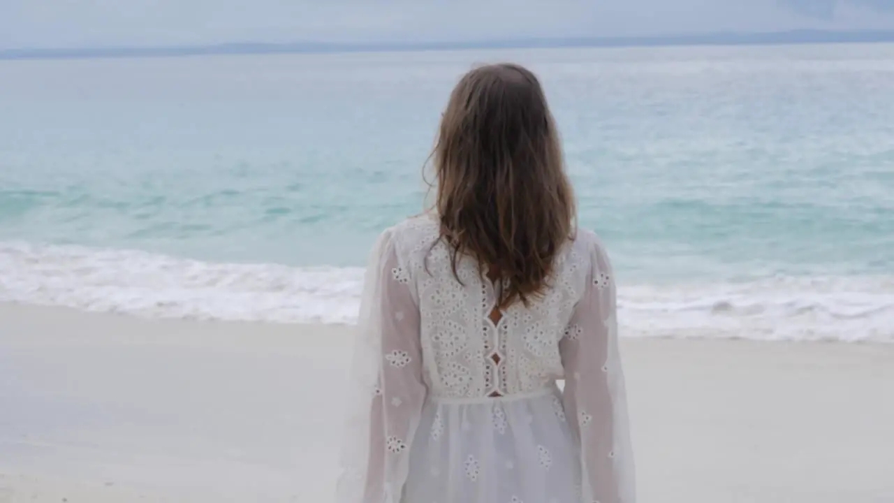 Ultra slow motion shot of woman with brown hair in white dress walking on beautiful beach looking at the ocean at Asu Island North Sumatra Indonesia