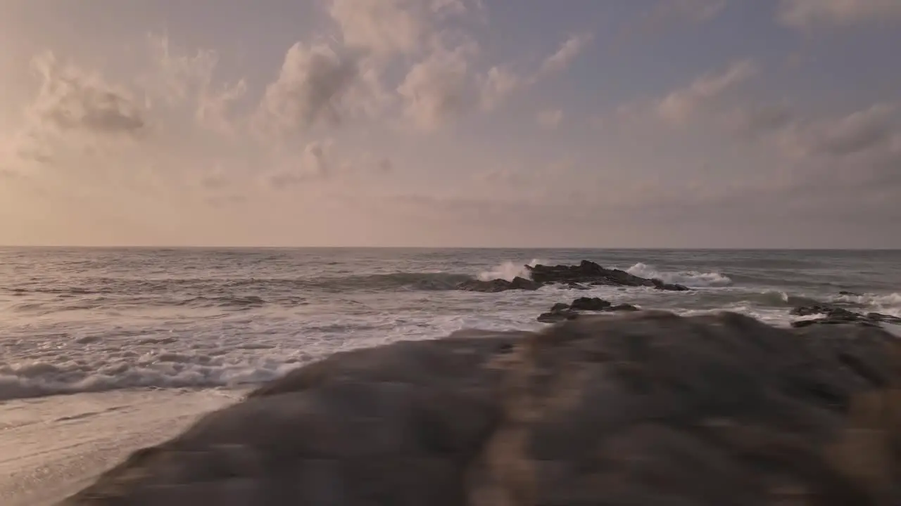 Rocky dramatic splashing waves on sunset coastal beach skyline dolly flying right