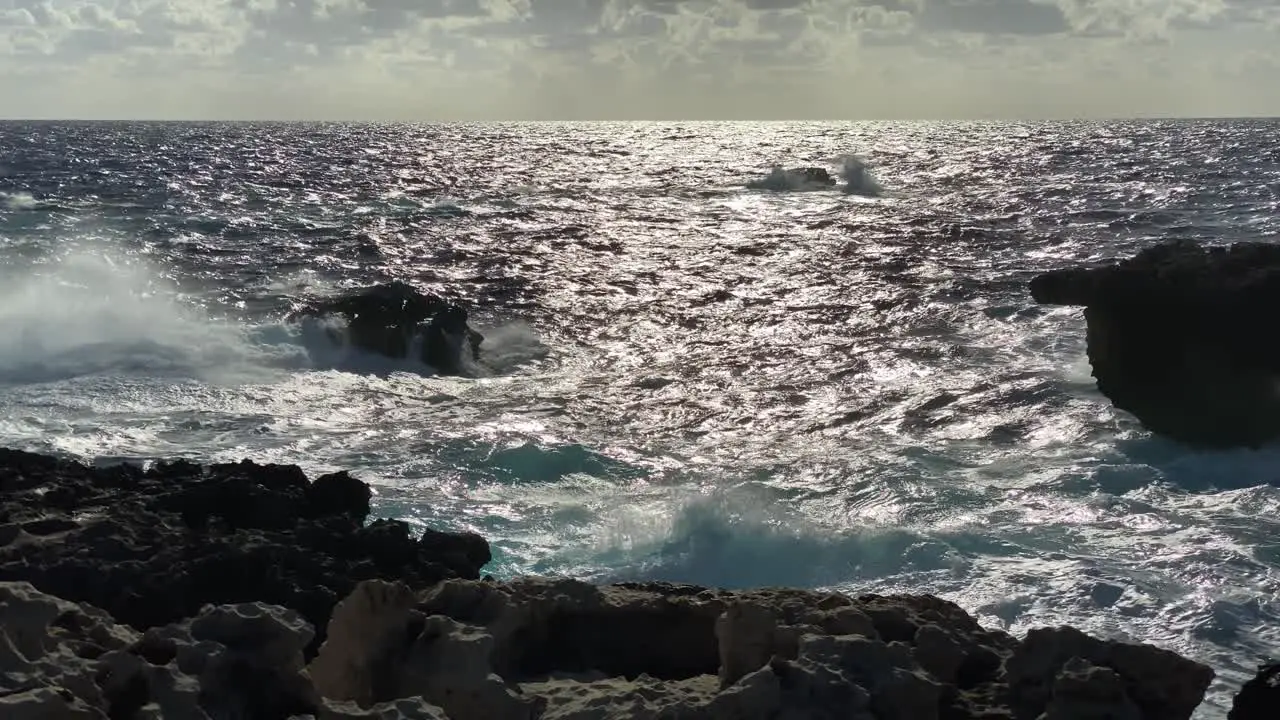 Sunlight reflects off blue ocean crashing against backlit rocky coast Gozo Malta