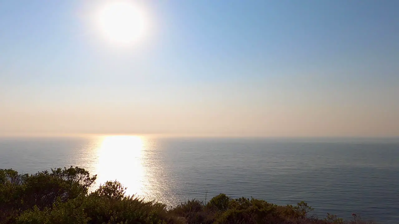 Slow zoom out of the sun beginning to set over the Pacific Ocean along the Northern California Cliffside on a warm summer afternoon 4K