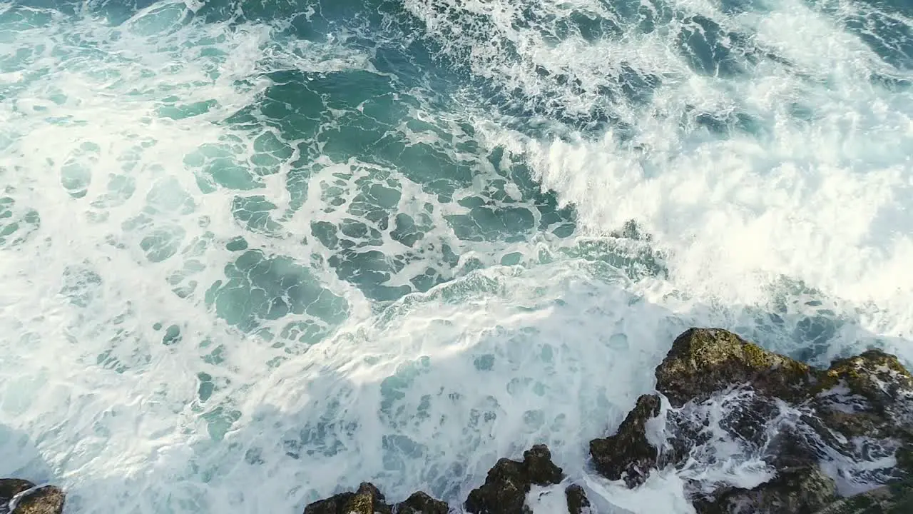 Aerial top-down backward over sea waves crashing on rocky coast near Najayo beach