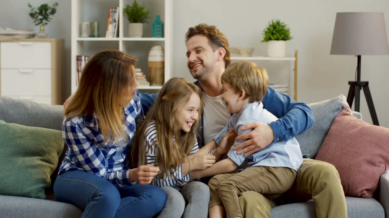 Mother Father And Their Children Having Fun On The Sofa In The Living Room Tickling And Laughing