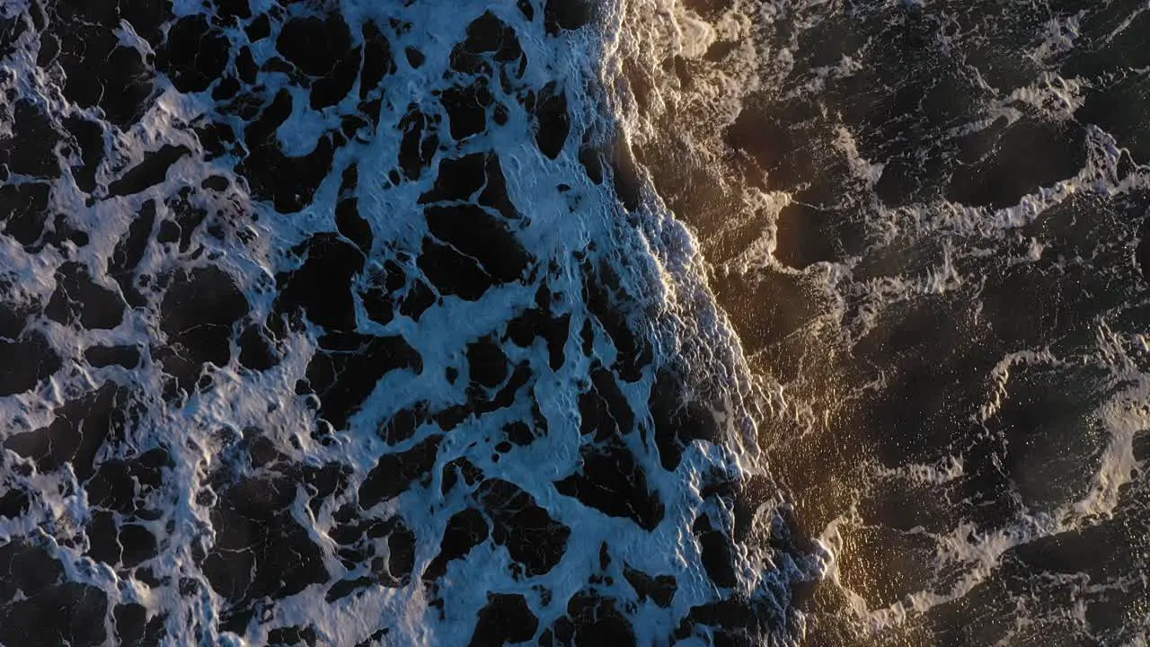 Aerial TOP DOWN flying slowly forward as a couple of wind whipped waves pass over a dark ocean with cool patterns in the surf in York Beach Maine