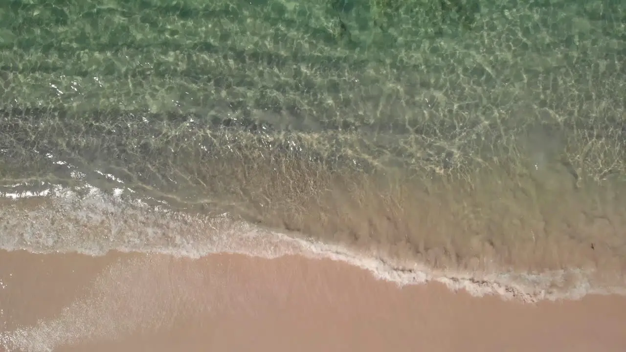 Aerial view above calm transparent sea water waves and a tropical beach birds eye drone shot