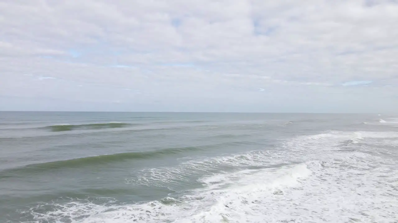 Aerial wide angle orbit low over big waves that crash toward the shore line of Muriwai beach New Zealand