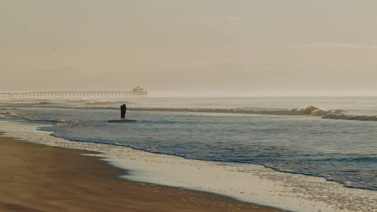 Wide shot showing mystic misty atmosphere at beach with crashing waves and jetty in background