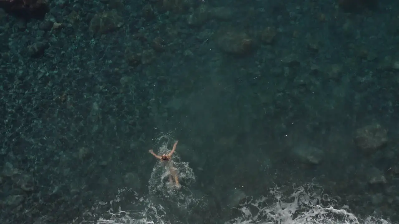 Fit woman in bikini on summer holiday walking into clear water jumping in going for a swim top down aerial