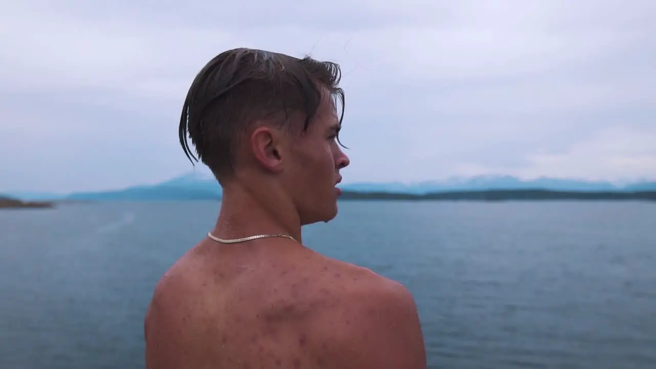 Slow motion shot of a young man with water dripping off of his face wearing a silver necklace staring into beautiful seascape taking in the moment and embracing the feeling of life and freedom