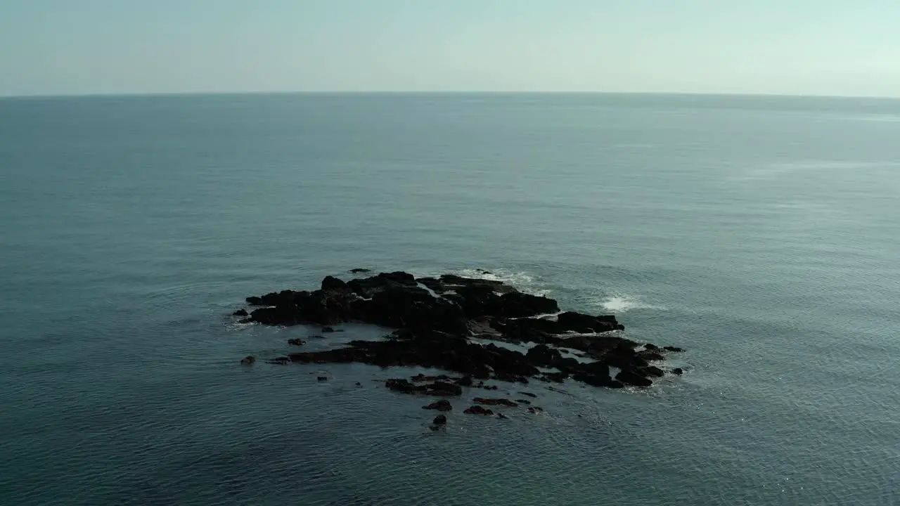 Aerial wide angle orbit of rocks on ocean water on calm day