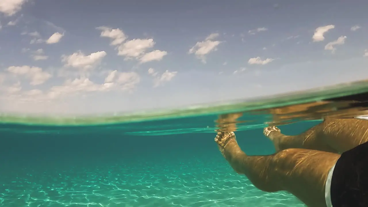 First person view of man legs and feet floating on beautiful clear and transparent ocean water of exotic island