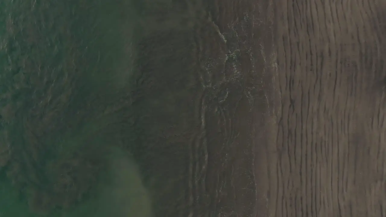 Aerial flight above empty beach with ocean sand swirls in Costa Rica