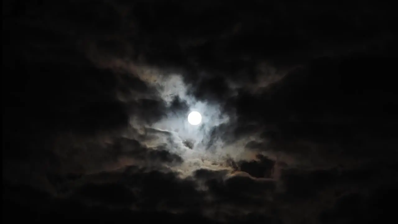 Wide time lapse of slowly rising full moon with halo behind clouds copy