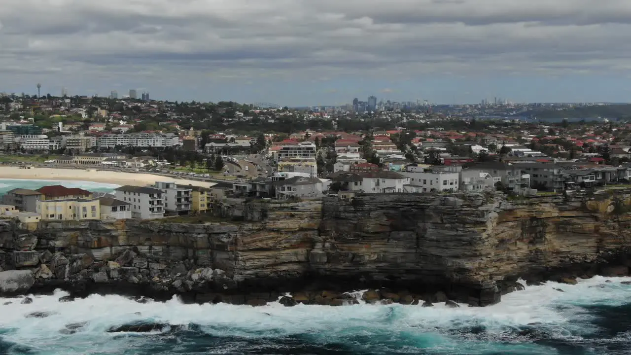 Waves crashing on rocky cliff of Ben Buckler Point with Bondi Beach in background Australia