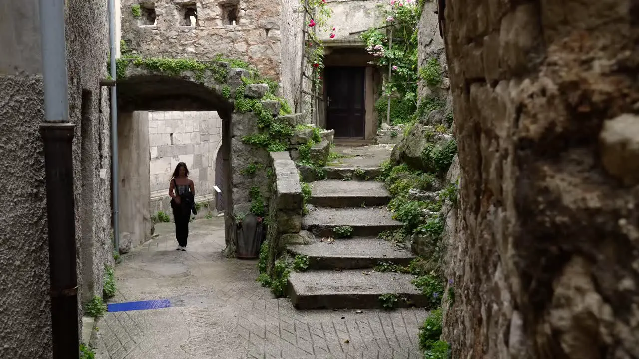 Young woman walks through an alleyway under an old stone building covered with vegetation