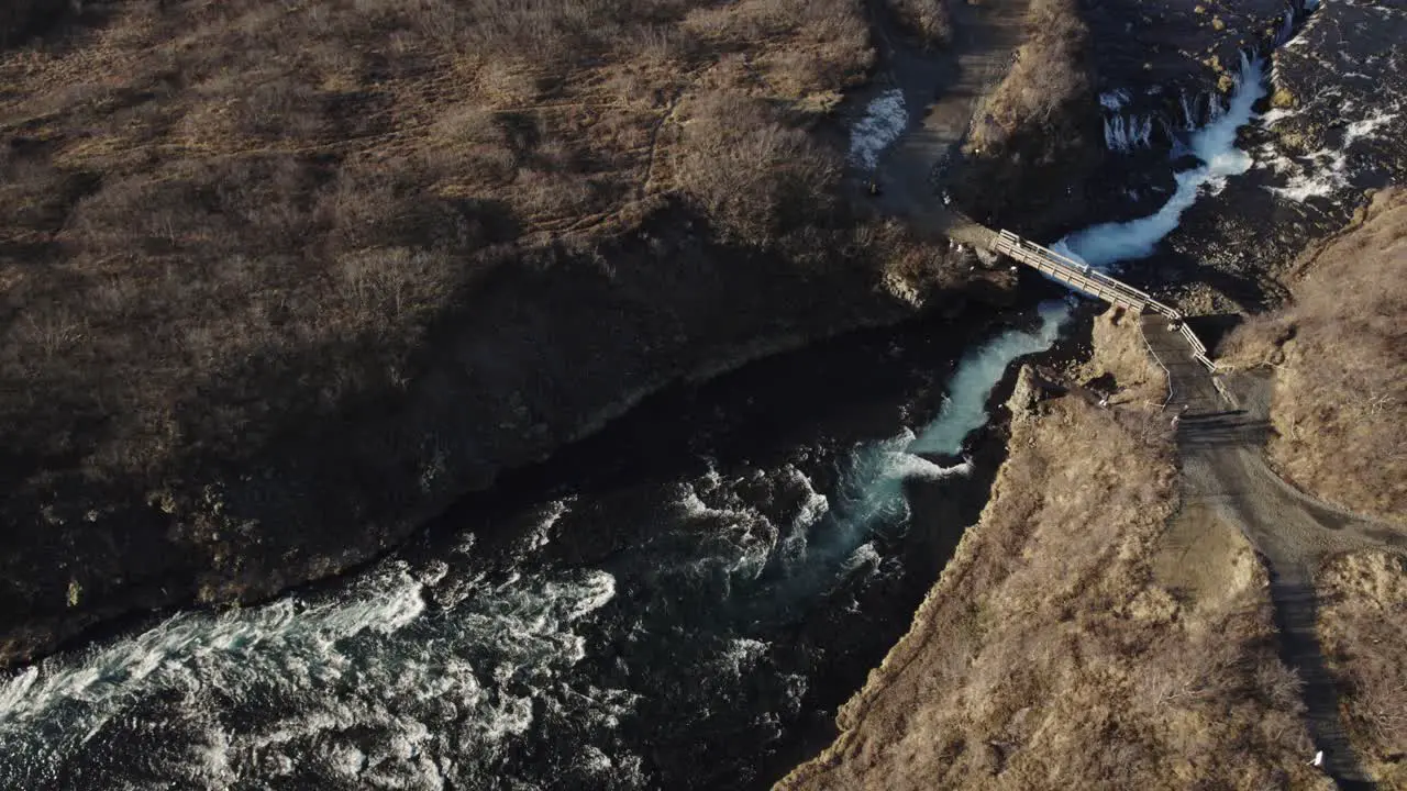 Impressive bridge over wild river and waterfall in vast volcanic landscape