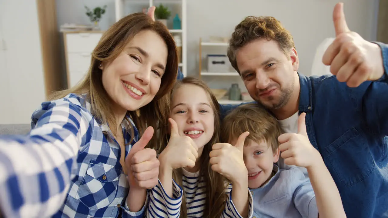 Pov Of The Cheerful Parents And Kids Sitting On The Couch In The Living Room Posing And Showing Gestures To The Camera