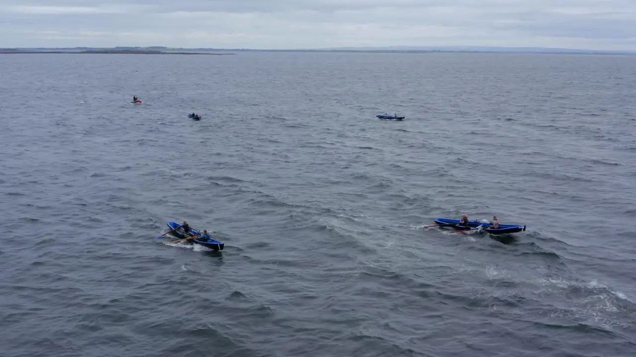 Drone descends over Currach boats racing across rocky ocean