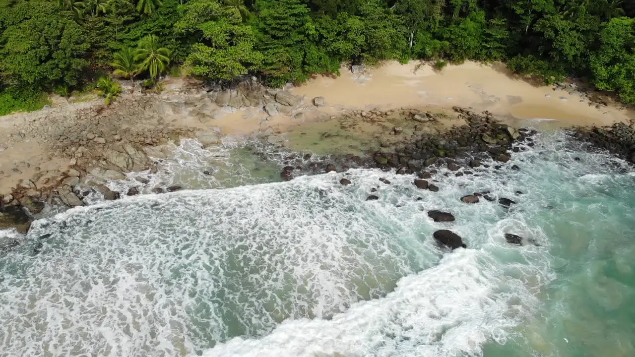 Turquoise Water Rocky Shore and Waves on a Wild Tropical Beach surrounded by Green Jungle and Trees