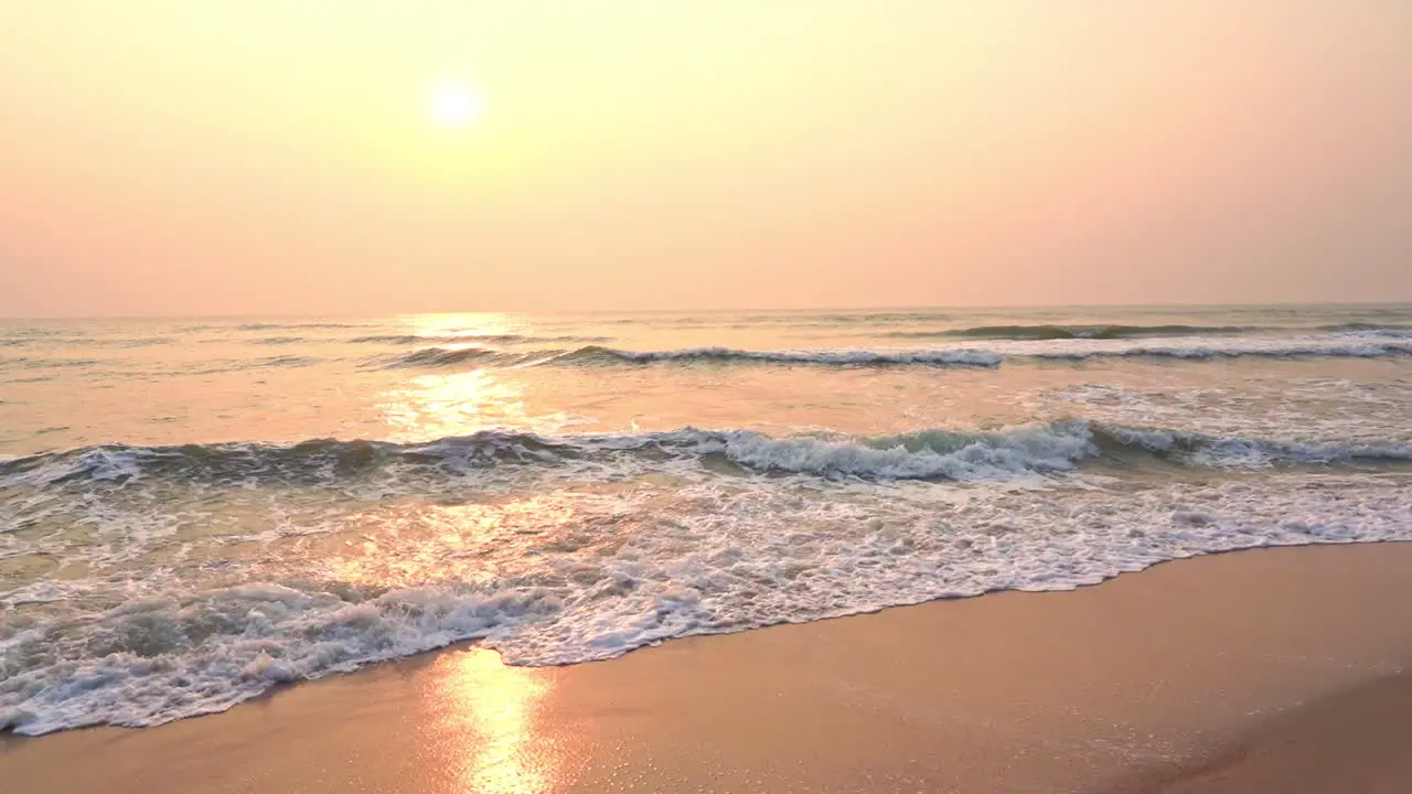 The sun sets as the surf rolls in on a deserted tropical beach