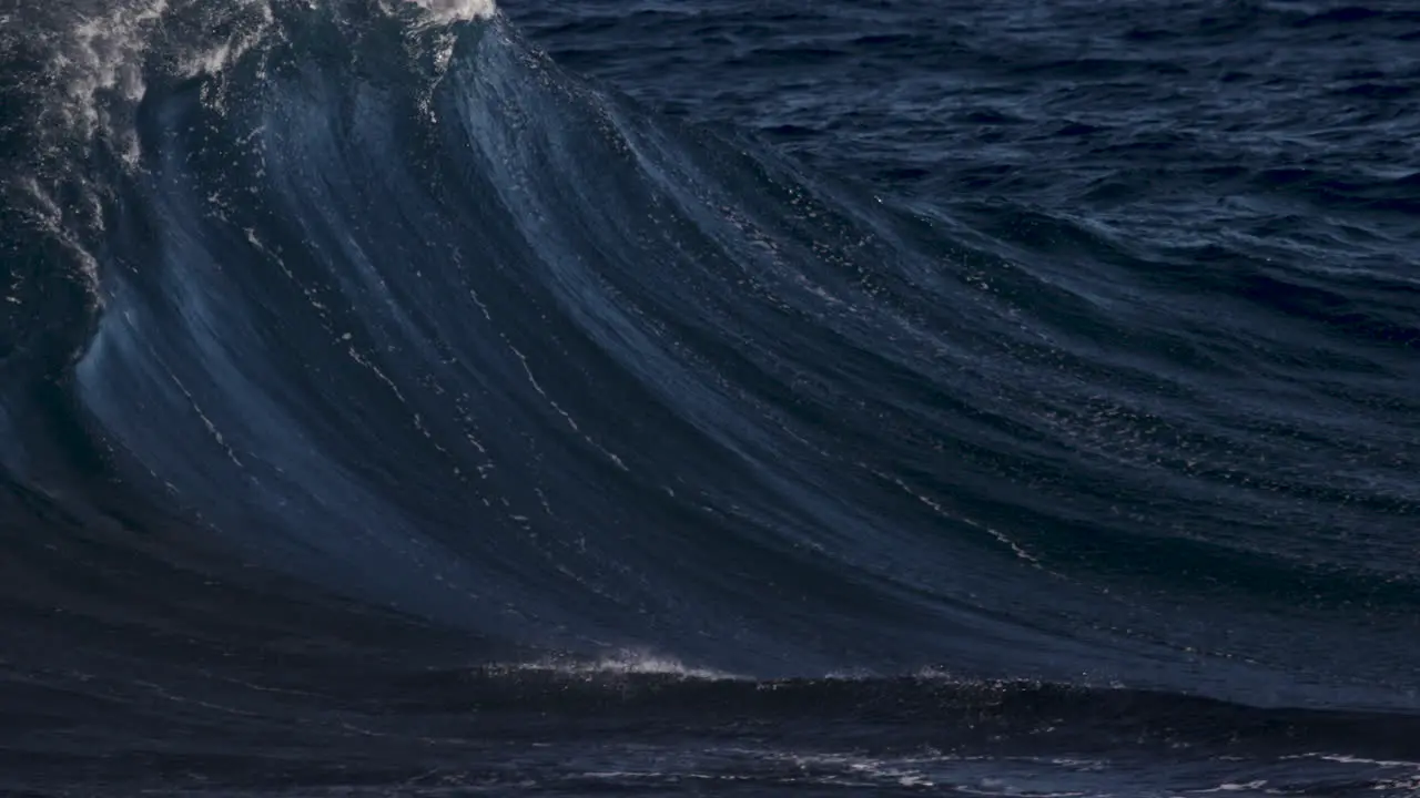 Wave breaking in slow motion on a sunny day as spray blows back up the wave face thanks to a strong offshore wind