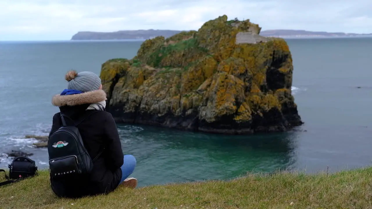 Person sitting on Ireland coastal cliff observing rocky coast shoreline formation ocean island