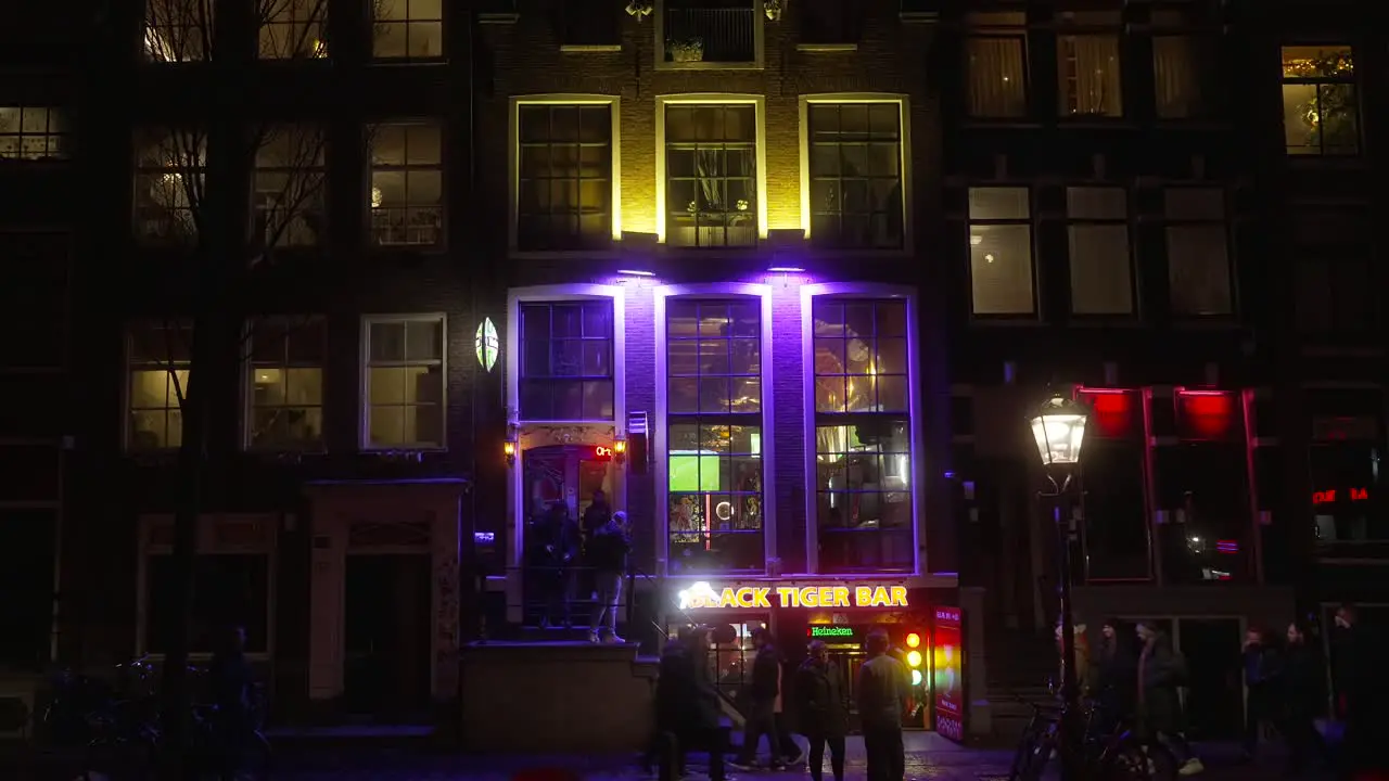 Static shot of The Black Tiger Bar in Amsterdam during nighttime pedestrians walking around city streets