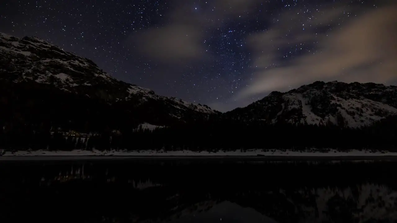 Night sky time lapse with snowy mountains reflected in alpine lake Italy