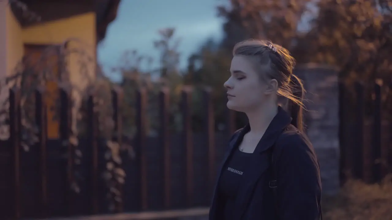 Girl with a pigtail walks behind the darkness on a street lit with lamps