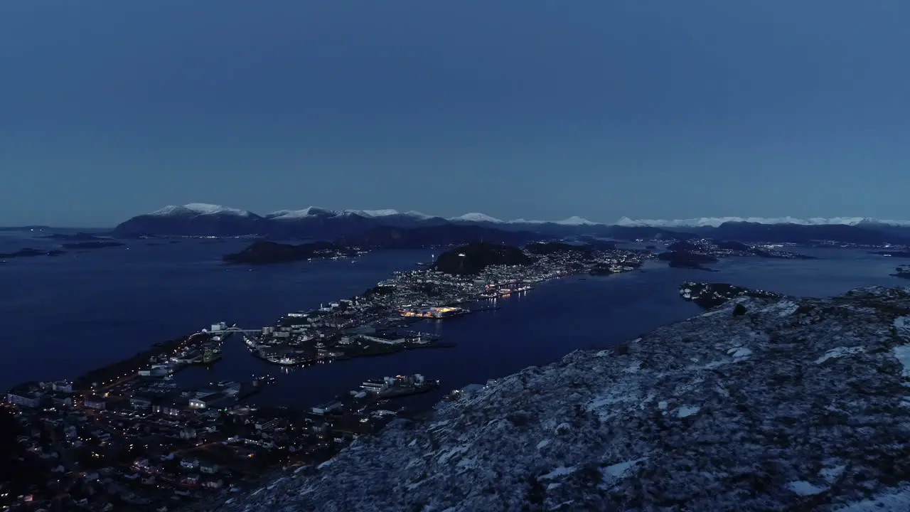 high aerial night shot of a city in the sea with many lights next to a mountain in winter