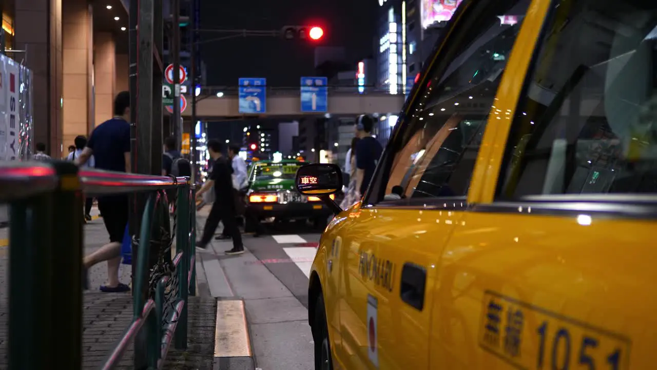 Tokyo taxi at night with the reflection of the taxi sign shot in the taxi’s wing mirror and passers-by in the background