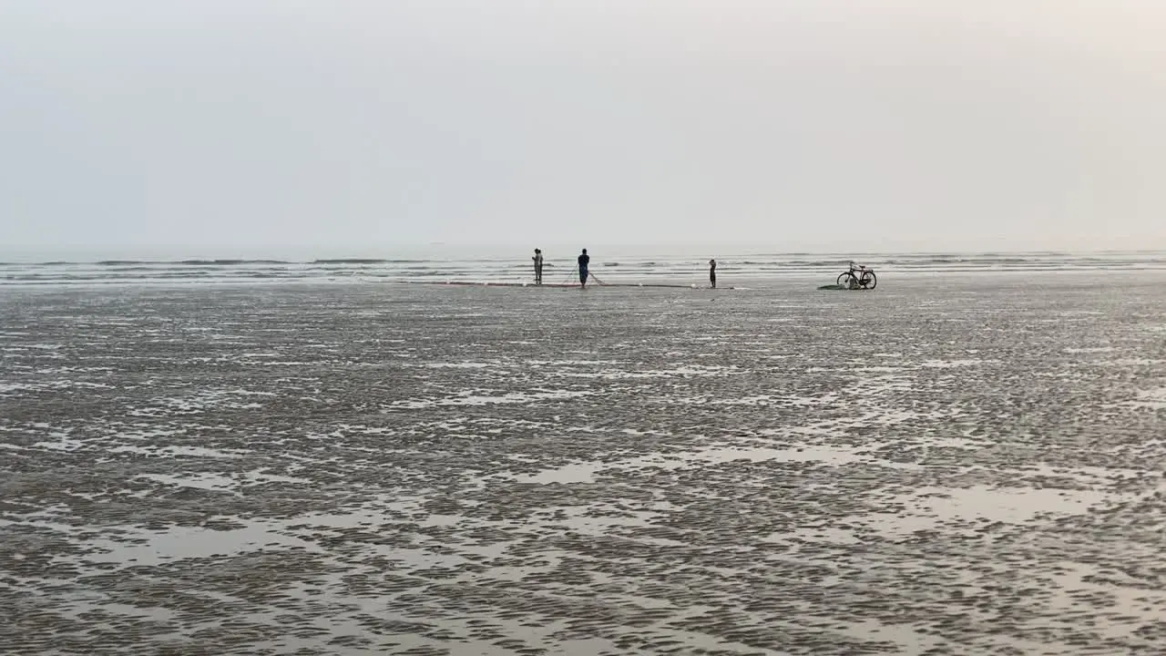 Distant silhouette view of an empty beach with fishermen working on fishing net and cycle parked aside in Bengal India