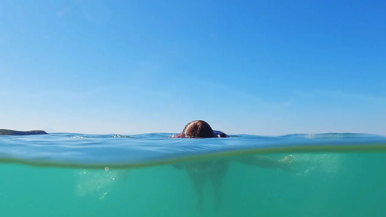 Young red-hair girl swimming undersea Half underwater view