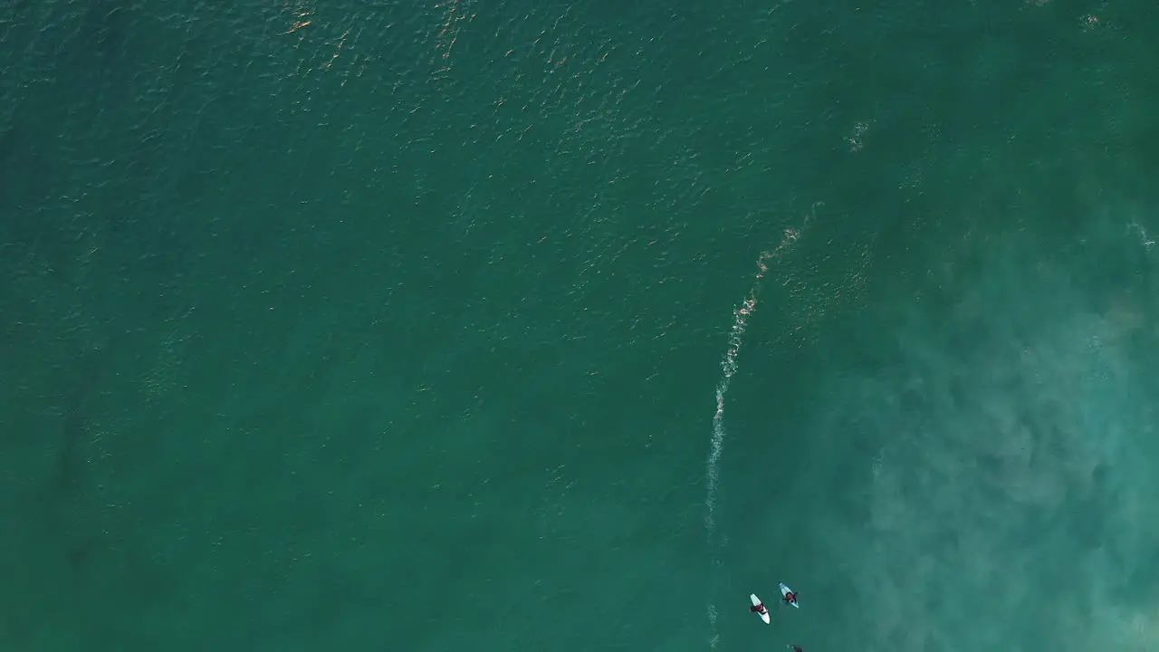 Aerial Vertical View Of Llandudno Beach With Surfers On Surfboards Floating In Turquoise Blue Waters