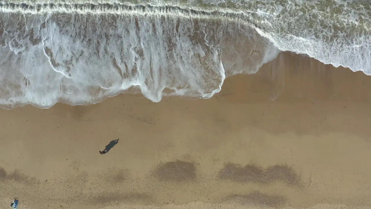 Aerial shot of couple with elongated shadows standing on a golden sand beach and admiring the sea