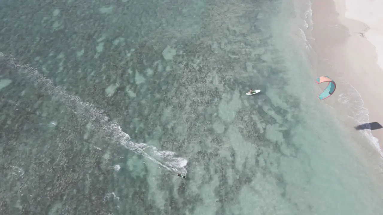 Aerial tracking shot of kitesurfer surfing on board close to beach In Pacific Ocean during sunny day Australia