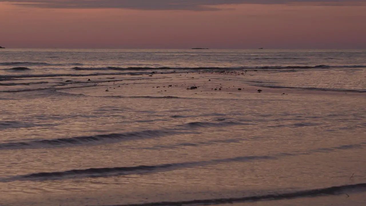 Shallow beach by low tide on golden hour with small waves covering the last visible part of the sand