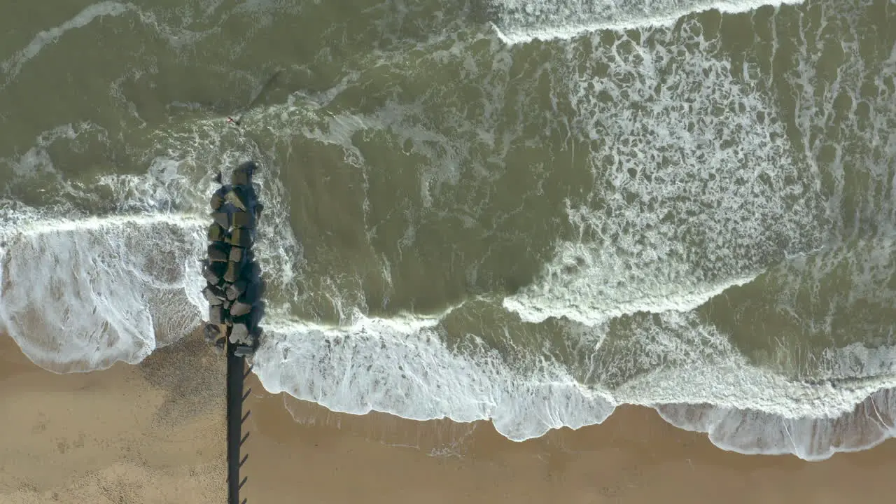 Aerial shot of the might sea and its waves crashing on a deserted golden sand beach