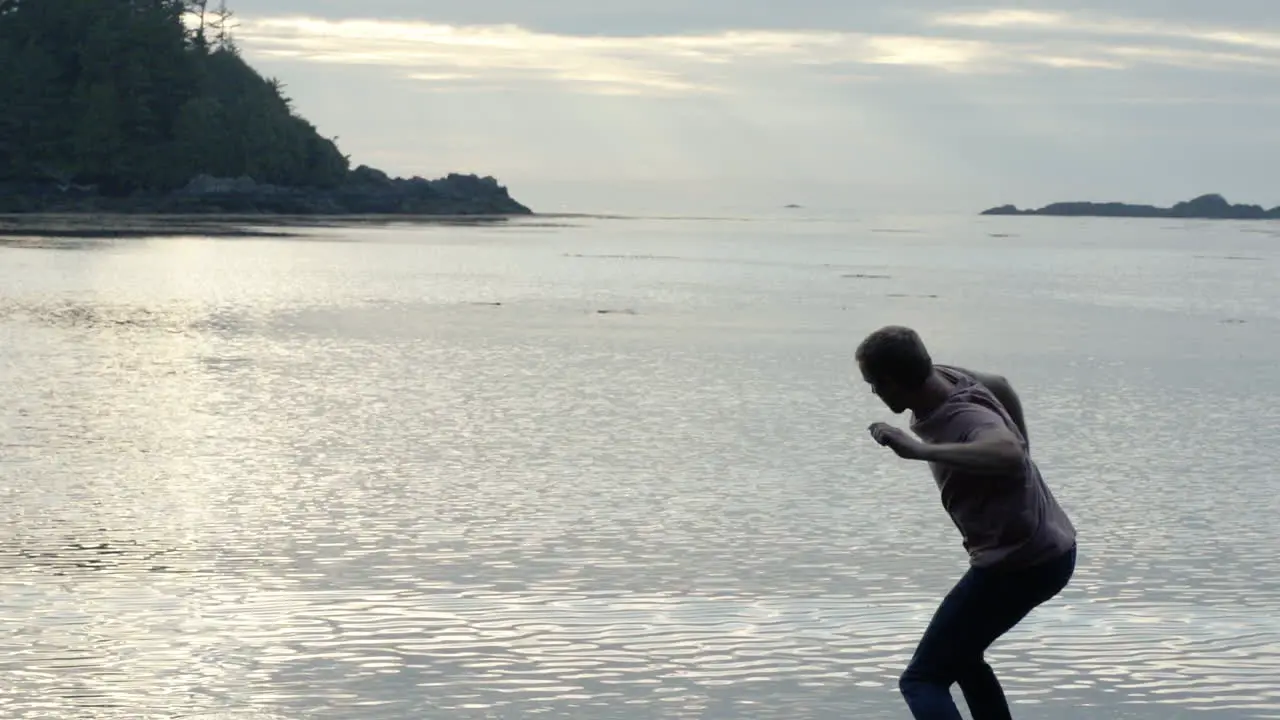 Slow motion man skipping rock on ocean beach and sunset