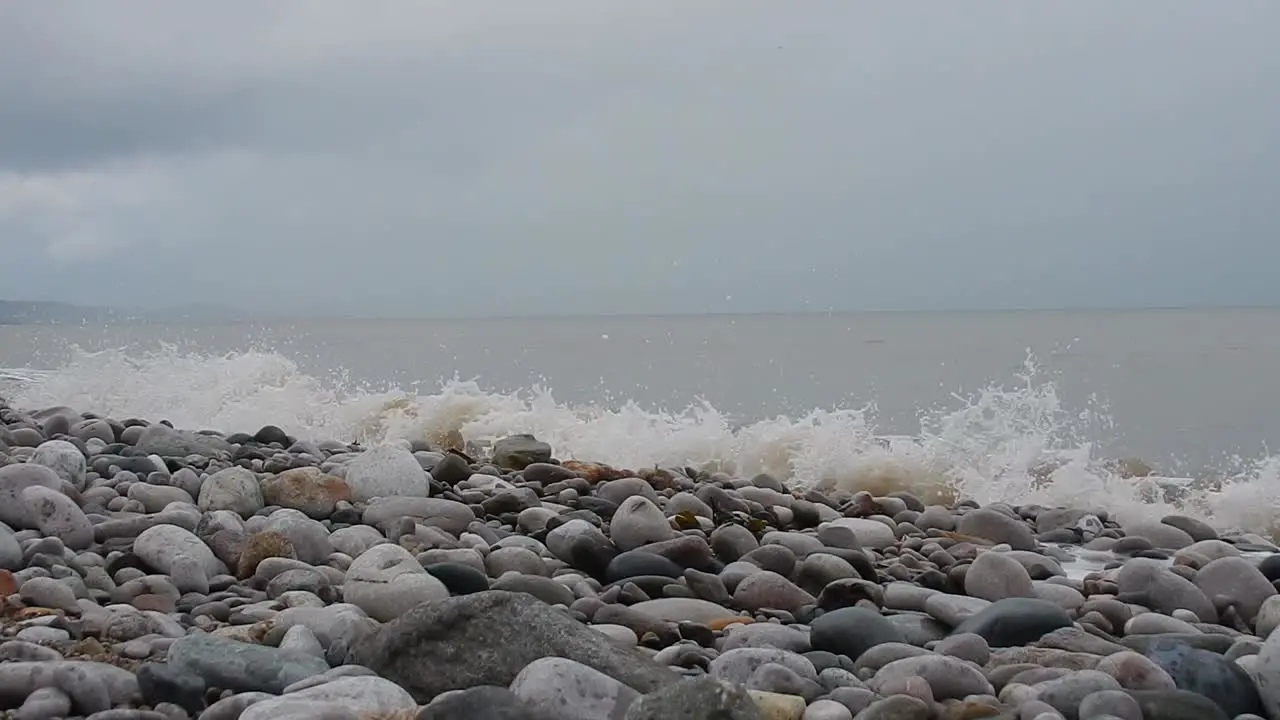 Foaming white waves washing into calming serene rocky pebble stone beach coastline