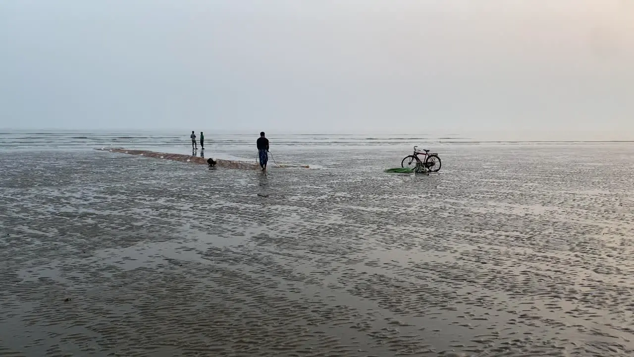 Silhouette gimble shot of a pleasant evening of the beach in India with fisherman standing near his cycle and working on his net