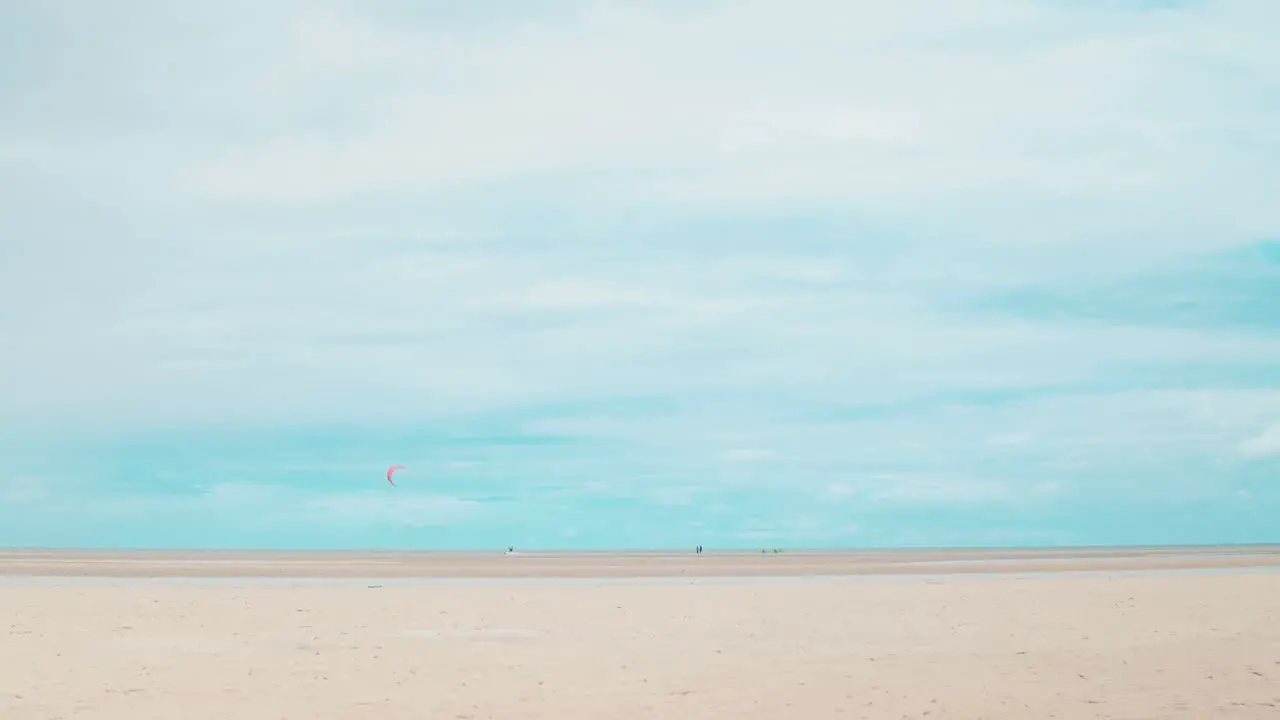 A kite surfer carves in the water of the low tide ocean in the distance whilst beautiful white clouds floating above perhaps brewing a storm