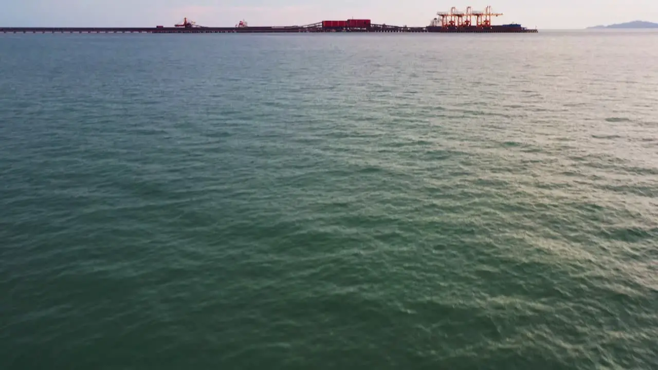 Aerial drone flyover Malaysian traditional fishing boat tilt up reveals export wharf of brazilian iron ore mining corporation teluk rubiah vale terminal along the horizon at dusk