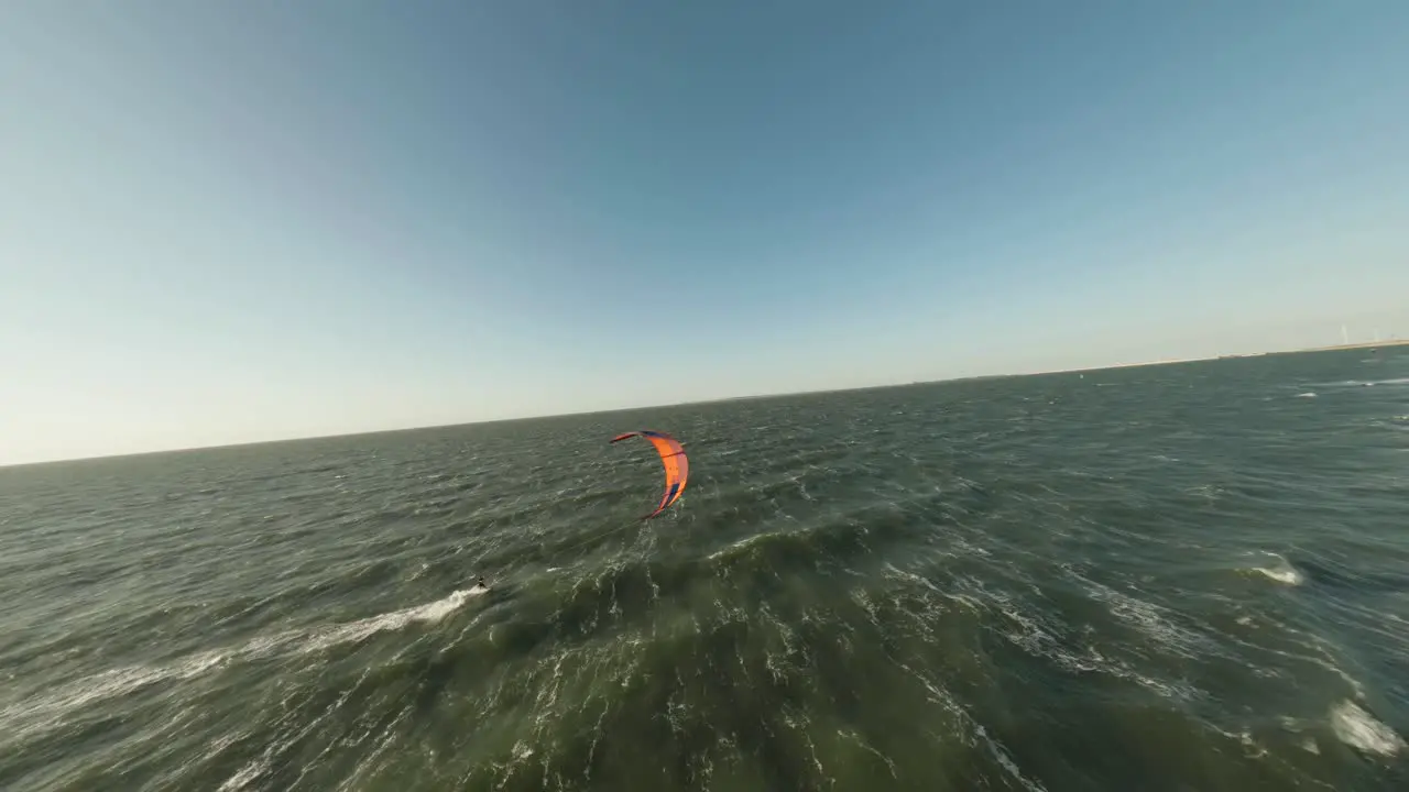 Aerial drone flight above wind kite surfer riding waves in strong wind