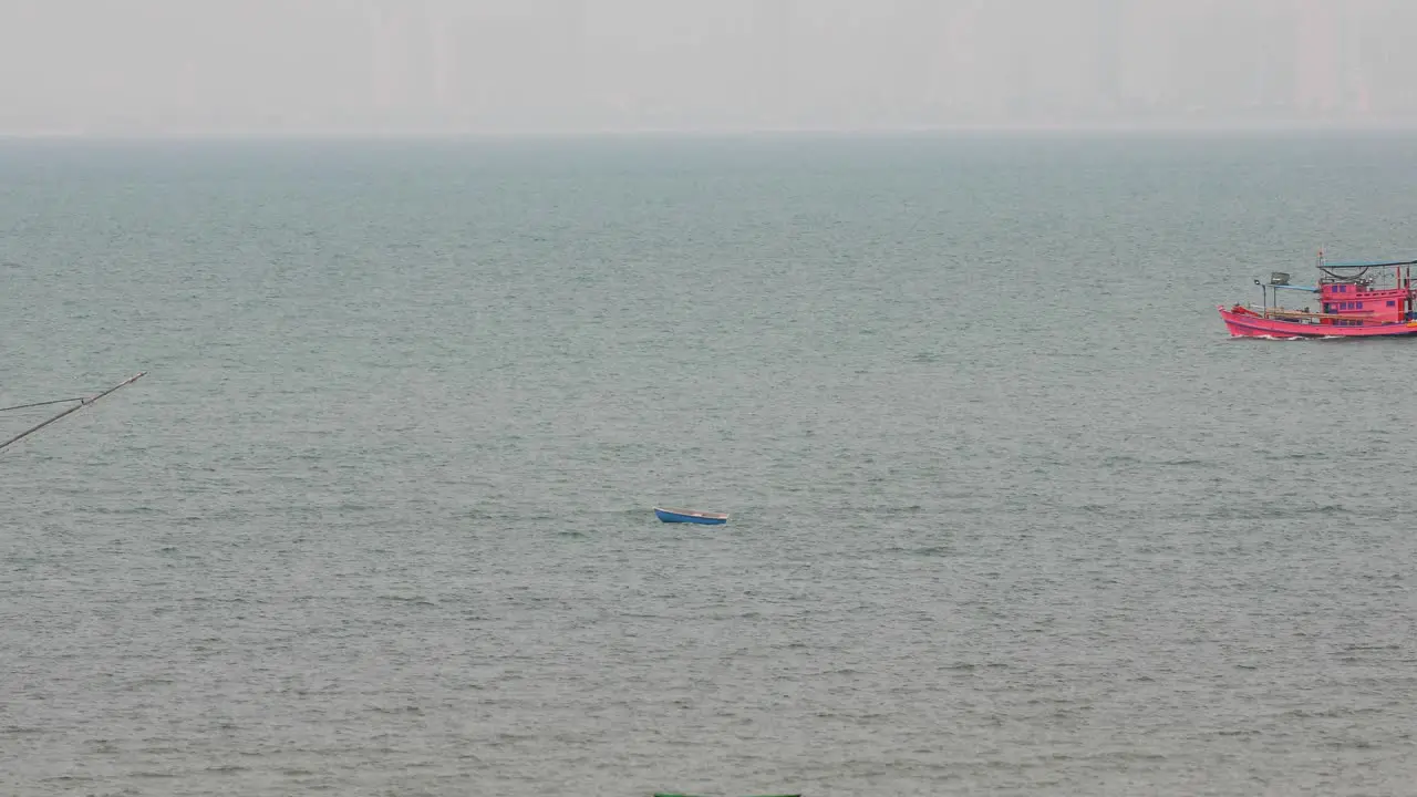 A Small Blue Boat Anchored with a Passing Thai Fishing Vessel in the Background off the Coast of Pattaya Thailand