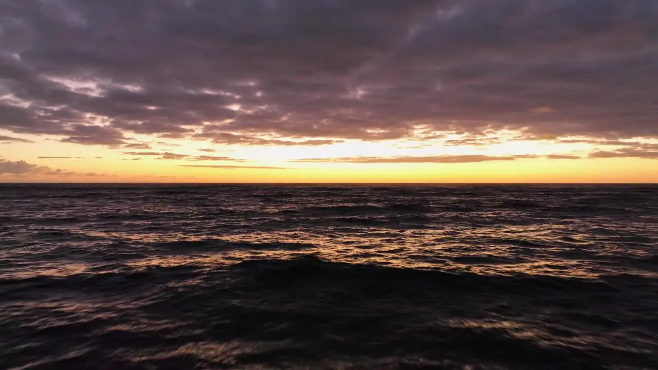 Flight over wavey sea in orange sunrise with pink clouds and sunlight