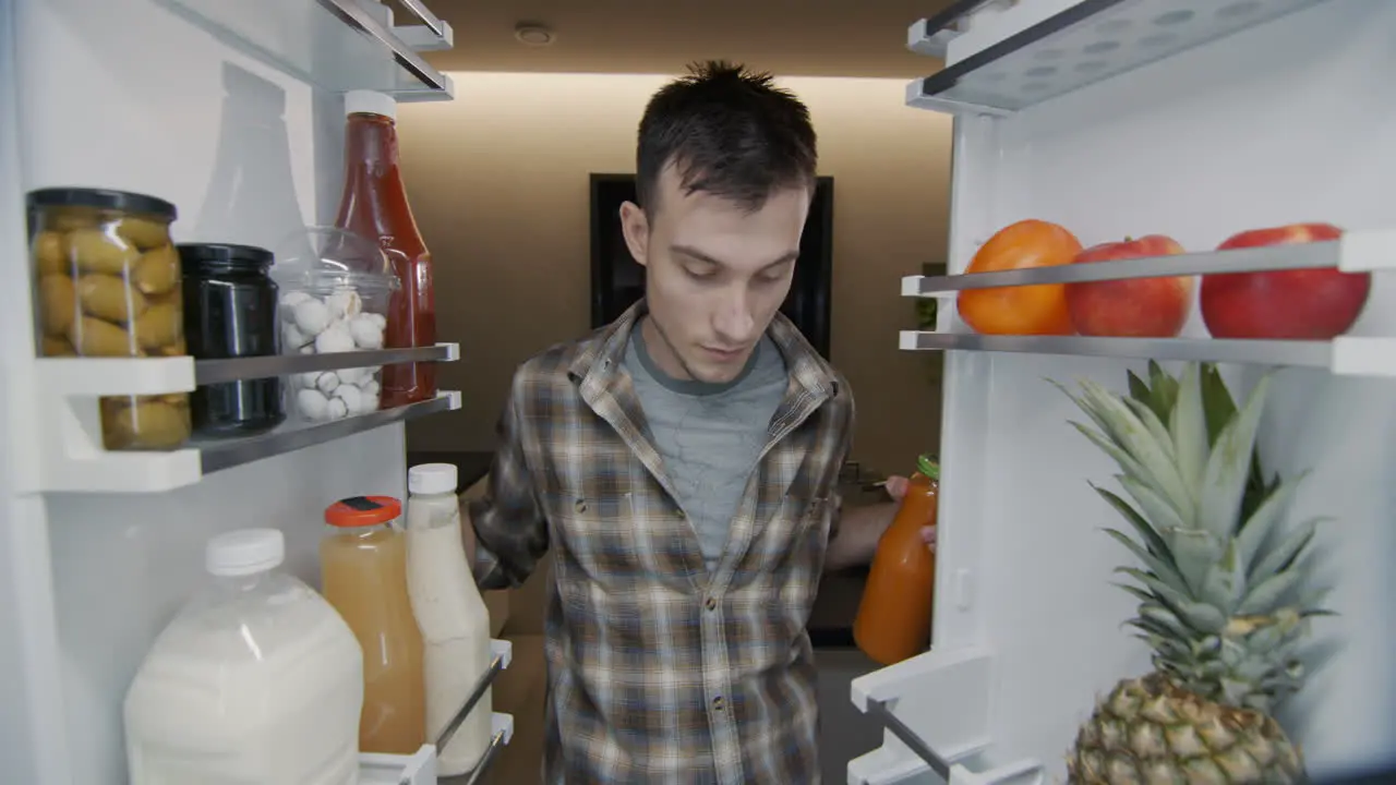 A young man takes a bottle of juice from the refrigerator View from inside the refrigerator