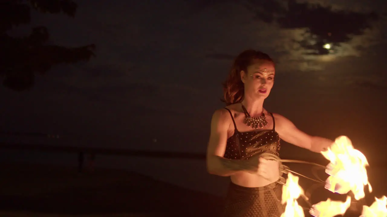 Woman Twirling And Waving Fire Fans Against Cloudy Moon Lit Sky Medium Shot Slowmo